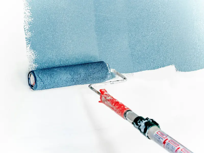 Farbrolle streicht eine Wand in gedecktem Blau